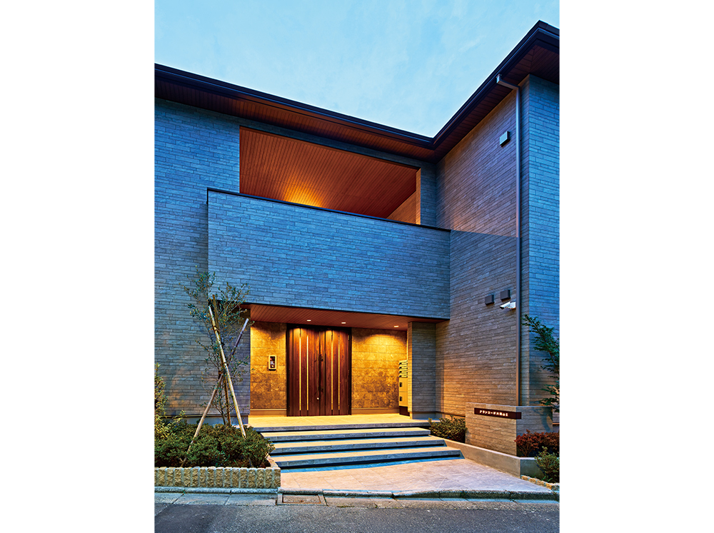 エントランス扉は重厚感のある両開きタイプ。ダークブラウンを選び、軒天井と色を揃えた。真上にあたる部分には入居者専用のコミュニティスペースを設置。